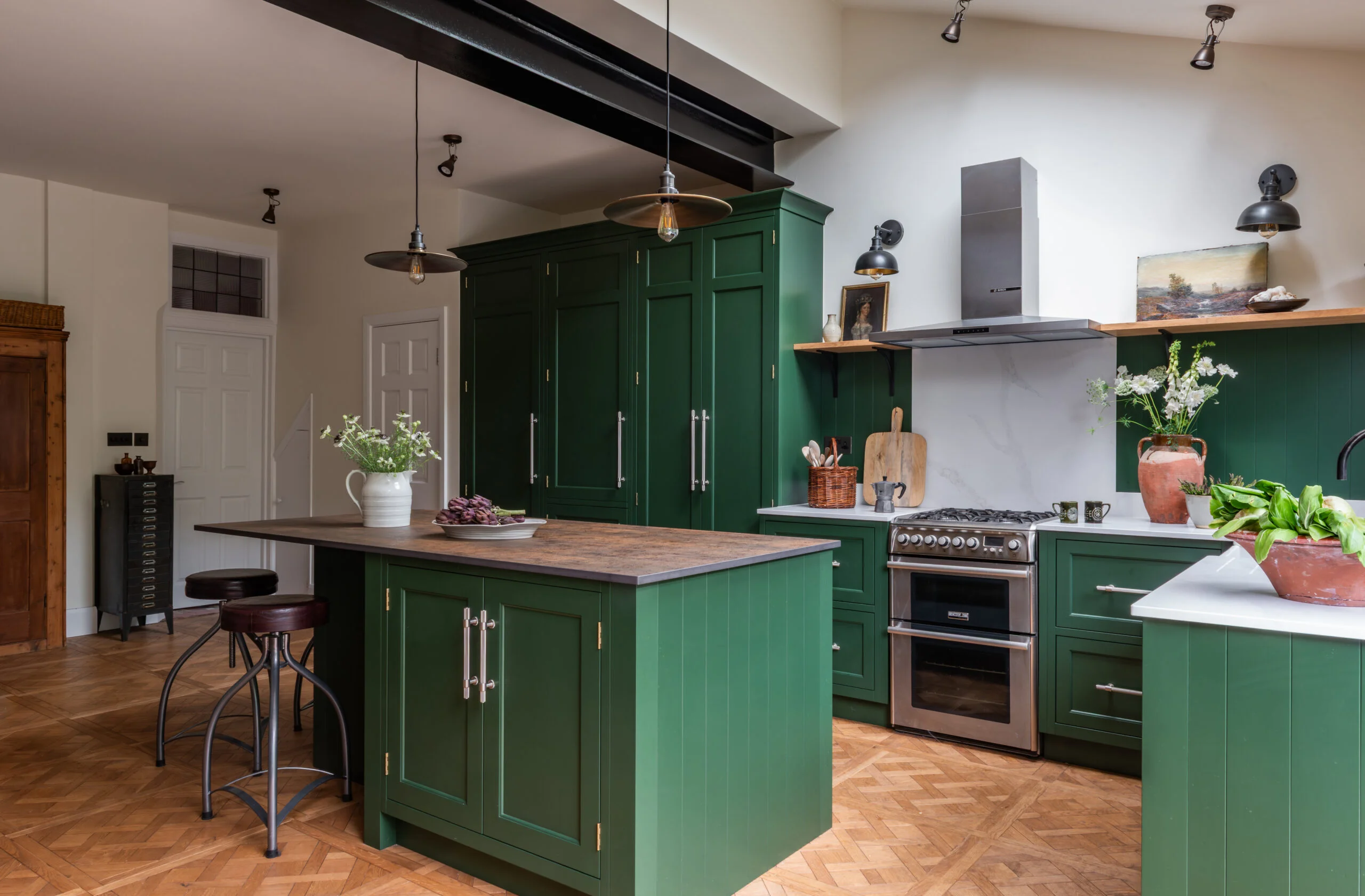 Green kitchen island at The Gables with two stools, cupboard storage and a clear worktop opposite the cooker